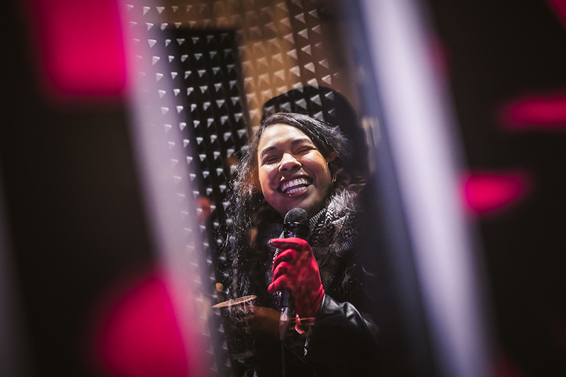 A woman with a red glove smiling while holding a microphone inside the Pop-up Karaoke pod